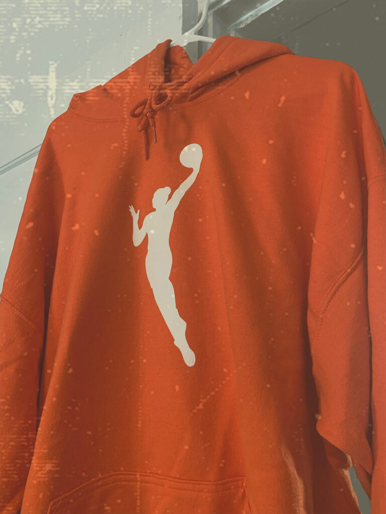 Photo of an orange WNBA logo hoodie on a hanger.