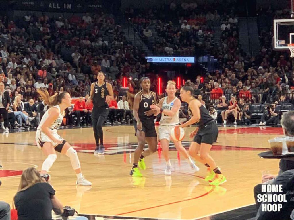 A photo of a live WNBA game between the Las Vegas Aces and the Connecticut Sun. Kelsey Plum of the Las Vegas Aces drives as her defender, Courtney Vandersloot of the New York Liberty, tries to get around a screen.