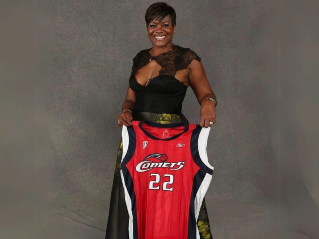 Sheryl Swoopes in formal dress, holds up her Houston Comets jersey.