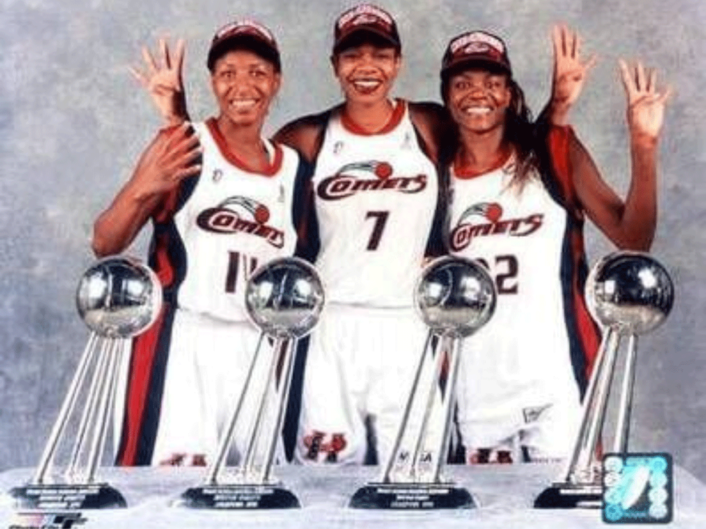 Cynthia Cooper, Tina Thompson, and Sheryl Swoopes stand behind their four WNBA championship trophies.